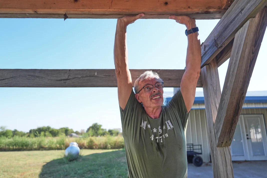 Ed Westrick uses his hands to move a wooden panel at the top of a frame structure made of wood.