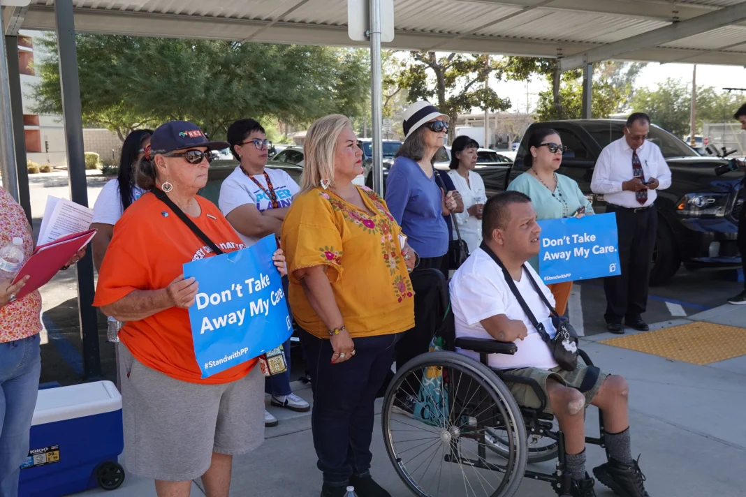 A group of about 10 people stand on a sidewalk. Some hold signs that say,